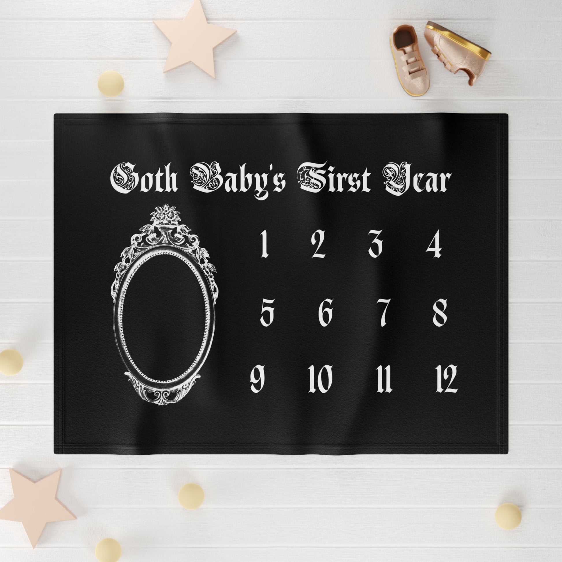 Black milestone blanket with silver crown design and numbers on a white wooden surface.